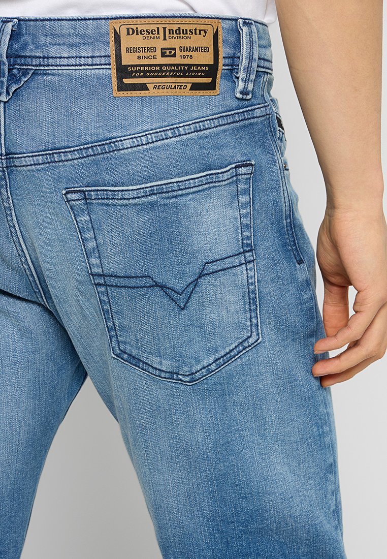 Verblasste blaue Denim-Jeans mit einem auffälligen, schrägen Design der Gesäßtasche und einem braunen Etikett am Bund, das Marken- und Pflegehinweise enthält.