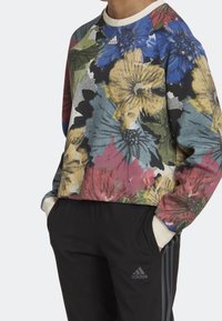 Sweatshirt à motifs floraux multicolores, avec un col rond et des manches longues, associé à un pantalon noir fuselé avec trois bandes.
