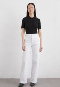 Zwart geribde poloshirt met korte mouwen en drie knopen, gecombineerd met witte wijde jeans en zwarte enkellaarsjes.