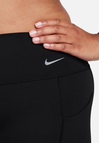 Svarte høytaljede leggings laget av elastisk materiale med en glatt tekstur, med en liten grå Nike-logo nær midjen.