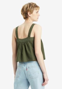 Top corto color verde oliva con spalline bordate in pizzo e schiena arricciata. Abbinato a jeans a vita alta di colore blu chiaro.