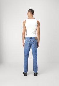 Camiseta blanca sin mangas para hombre con jeans de mezclilla azul. Los jeans tienen un corte clásico y bolsillos traseros visibles, combinados con zapatos negros.