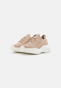 Ljusbeiga sneakers med en texturerad stickad ovandel, elastiska snören och en kraftig vit sula. Rund tå och subtil branding på tungan.