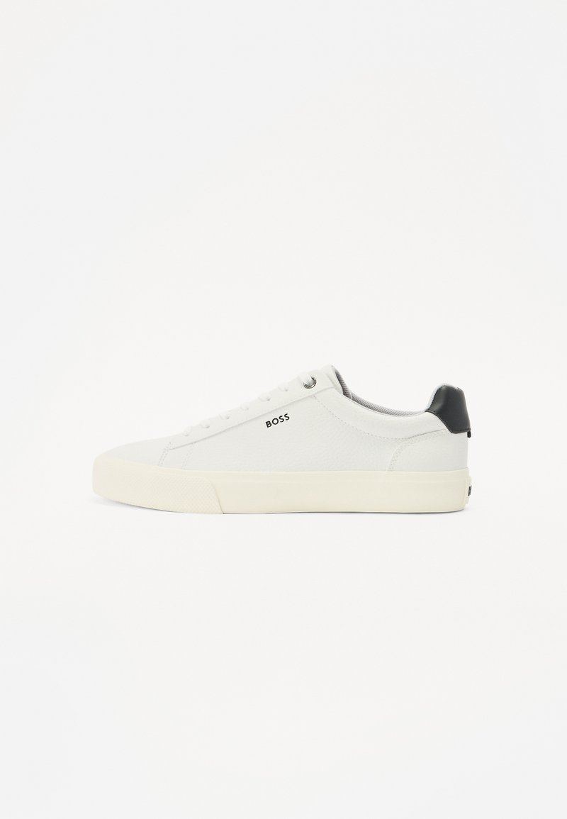 Vita lädersneakers med en texturerad yta, featuring en svart hälkappa, rund tå och logotyp på sidan i svart. Lätt gummisul.