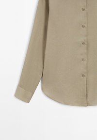 Camicia beige a maniche lunghe con una texture liscia, chiusura con bottoni davanti e orlo arrotondato. Presenta un colletto sagomato e dettagli ai polsini.