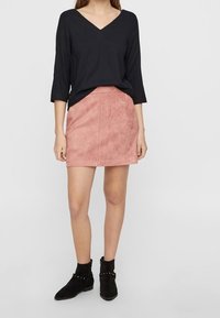 Top negro de manga larga con escote en V combinado con una mini falda de ante rosa. Botines negros con tachuelas. Diseño simple, textura suave.