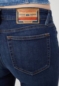 Mörkblå denimjeans med orange sömmar och en rektangulär läderlapp på midjan som har varumärkesinformation och text.