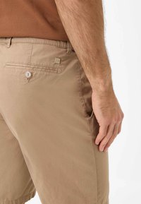 Lysbrune shorts lavet af struktureret stof, med en baglomme med knaplukning og en lille metal logo-accent.