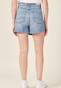 Shorts de mezclilla en azul claro con un lavado desvanecido, que presentan bolsillos traseros, cintura alta y dobladillo sin acabar. Llevados con zapatillas altas blancas.