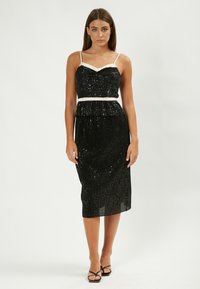 Vestido negro de lentejuelas con figura ajustada, escote crema y cinturilla. Diseño de longitud media con un acabado texturizado y tirantes finos.