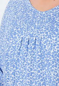 Blouse met blauw-wit patroon, voorzien van een v-hals, plooien in het midden en een zachte stoftextuur. Het ontwerp bevat een verspreide bloemenprint.