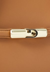Sac à main en cuir beige avec une texture lisse. Présente un fermoir en doré avec un détail de logo. Design simple, forme rectangulaire.