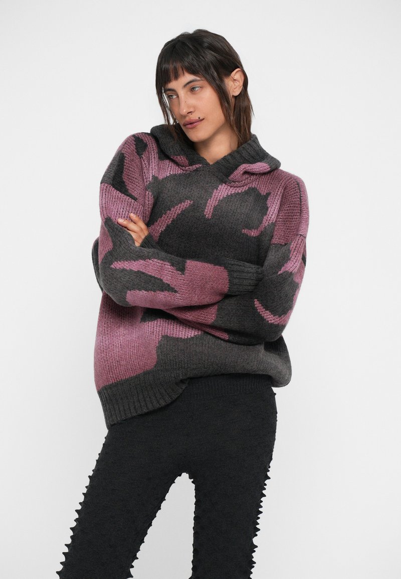 Maglione con cappuccio a maglia caratterizzato da un motivo astratto grigio e rosa, polsini a costine e una vestibilità rilassata. Indossato con leggings neri texture.
