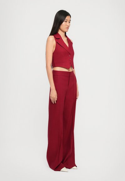 Rotes, ärmelloses Oberteil mit Reverskragen und zwei Knöpfen, kombiniert mit hoch taillierten, weit geschnittenen roten Hose. Glatte Textur, schmale Silhouette.