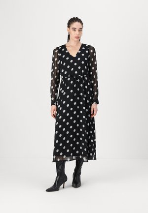 Rochie neagră cu buline albe, cu mâneci lungi transparente, decolteu în V, talie legată și fustă fluidă. Asortată cu cizme negre cu toc, până la genunchi.
