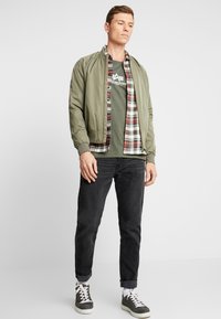 Maslinzasta bomber jakna preko plaid flanel košulje, maslinaste majice, crnih traperica i sivih tenisica s bijelim vezicama. Jednostavan i ležeran outfit.