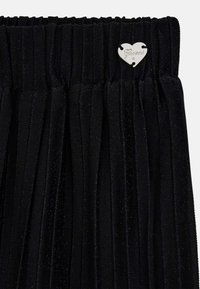 Tessuto nero plissettato con una piccola targhetta metallica a forma di cuore argentata incisa con la scritta "Guess" vicino al bordo superiore.