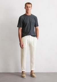 Grau strukturiertes kurzärmeliges T-Shirt, kombiniert mit cremefarbenen Leinenhosen, die einen Kordelzugbund und umgeschlagene Säume aufweisen, abgerundet mit beigen Schuhen.