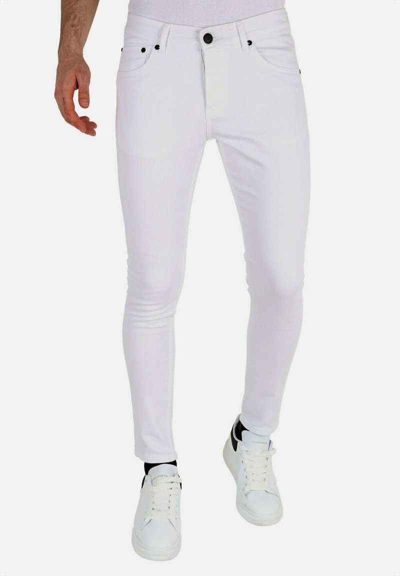 Witte slim-fit jeans van denim, met vijf zakken, zwarte knoopsluiting, en gedragen met witte sneakers en zwarte sokken.