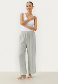 Gestreifte, leichte, locker sitzende Hose aus grauem und weißem Stoff mit elastischem Taillenbund und Kordelzug. Kombiniert mit einem weißen Tanktop.
