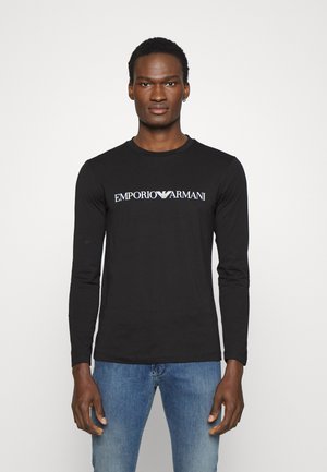 Black long-sleeve shirt featuring "EMPORIO ARMANI" logo in white across the chest. Made of soft material, fitted design.