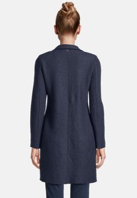 Langer Navy-Mantel aus strukturiertem Stoff. Verfügt über einen Kragen, lange Ärmel und eine gerade Passform, mit einem Knopfdetail am Hals.
