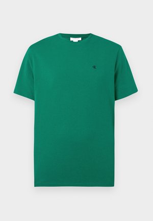 T-shirt verde a maniche corte con colletto tondo, con piccolo logo "cK" ricamato sul lato sinistro del petto, sfondo semplice.