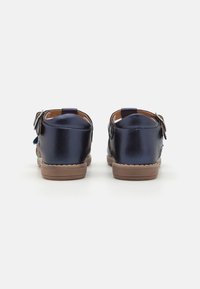 Mörkblå läderskor med en slät yta, med detaljer i form av rem och spänne, samt en ljusbrun gummisula. Bakifrån visad.