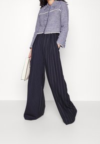 Avkortad, texturerad blå jacka med fransade kanter; tillsammans med högmidjade, flödande navy-byxor med vertikala vita ränder.