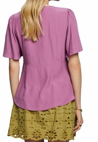 Blusa a maniche corte di colore lavanda, con una trama liscia e scollatura rotonda, abbinata a una gonna verde chiaro con aperture floreali.