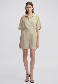Combinaison en lin beige à manches courtes avec un col, un devant boutonné, une taille cintrée et un short qui arrive au milieu des cuisses.
