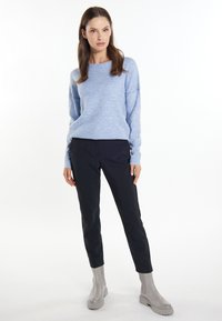 Lichtblauwe gebreide trui met een brede ronde halslijn, gecombineerd met zwarte slim-fit broek en grijze enkellaarzen met een stevige zool.