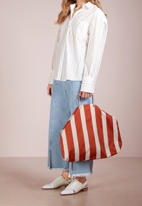Borsa a spalla a righe rossa e crema, grande, in tessuto con forma arrotondata. Abbinate a una camicia a righe bianche e una gonna di jeans.