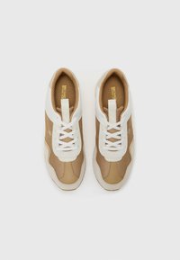 Tann- und weiße Turnschuhe mit Mesh-Einsätzen, strukturierten Gummisohlen, flachen weißen Schnürsenkeln und einem kleinen Logo an der Seite. Glatte Lederakzente sind ebenfalls enthalten.