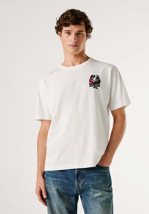 Wit katoenen T-shirt met korte mouwen, voorzien van een kleurrijke geborduurde afbeelding op de linkerborst en een ontspannen pasvorm. Gecombineerd met een blauwe spijkerbroek.