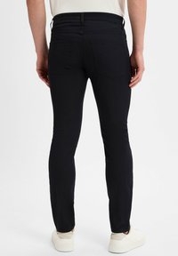 Czarne dżinsy slim fit o gładkiej fakturze, z dwoma tylnymi kieszeniami i paskiem w talii. Stylizowane z białymi trampkami i jasną koszulą.