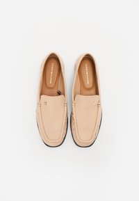 Beige læder slip-on sko med glat tekstur, tilpasset syning og sål i sort gummi. Har et lille logo på overdelen.