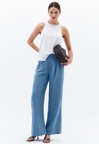 Witte mouwloze top, losse lichtblauwe brede pijpen, zwarte clutch en zilveren hakken. Glad stof en ontspannen pasvorm.