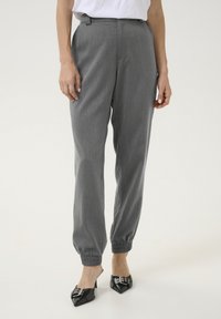 Pantalons gris fuselés avec une taille élastique et des chevilles resserrées, présentant une texture subtile et une coupe lisse et ajustée. Assortis à des escarpins noirs.