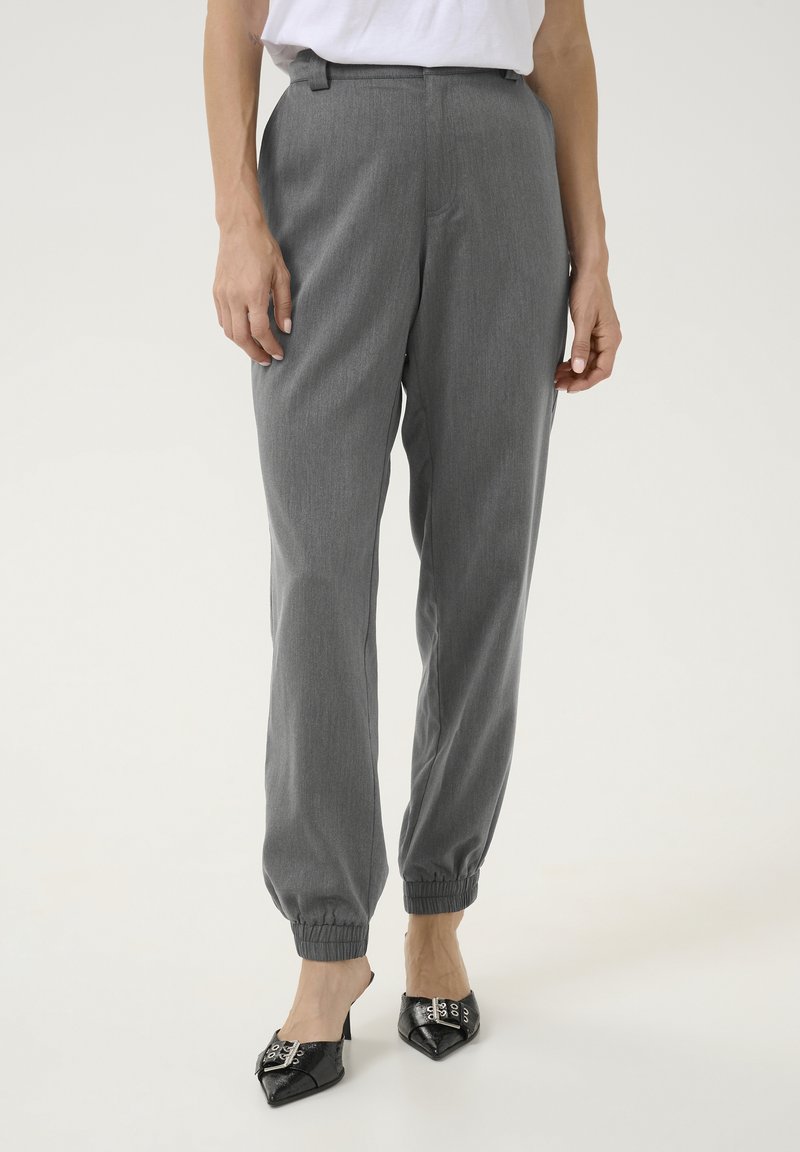 Pantalons gris fuselés avec une taille élastique et des chevilles resserrées, présentant une texture subtile et une coupe lisse et ajustée. Assortis à des escarpins noirs.