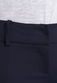 Gros plan sur la ceinture de pantalon bleu foncé avec une passante de ceinture sur une chemise en tissu blanc texturé.