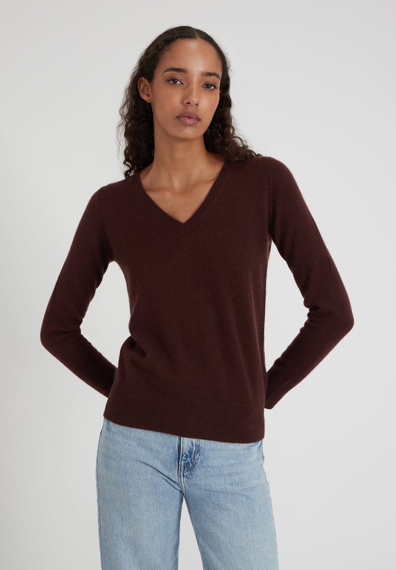 Pull en V bourgogne en tricot doux, avec des manches longues et un ourlet côtelé, assorti à un jean en denim bleu clair.