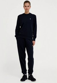 Granatowy komplet z bluzy i spodni, wykonany z miękkiej tkaniny; posiada ściągacze przy mankietach i małe logo na piersi.