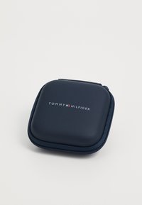 Tumedat sinine kõva kest, millel on lukuga sulgemine, sile tekstuur ja esipaneelil reljeefne 'TOMMY HILFIGER' logo.
