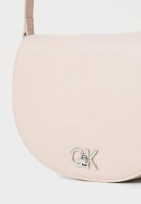 Borsa crossbody rotonda di colore rosa tenue, realizzata in pelle liscia con un accento del logo argentato. Presenta un design minimalista e una tracolla regolabile.