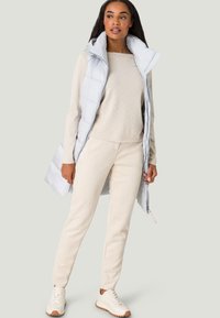 Light gray sleeveless puffer vest over cream textured sweater, paired with beige pants and light sneakers. Simple design, soft textures.