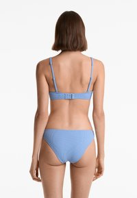 Modri bikini set z teksturiranim materialom, tankimi nastavljivimi naramnicami in zaponko na hrbtu zgornjega dela, skupaj z usklajenimi spodnjimi hlačkami z nizkim pasom.