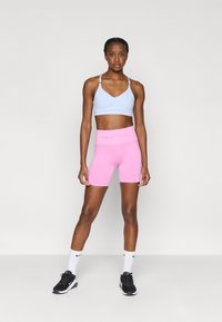 Αθλητικό σουτιέν σε ανοιχτό μπλε και ροζ σορτς Nike Pro, εφαρμοστά και ελαστικά υλικά, με λογότυπο στο σουτιέν και στη μέση. Μαύρα αθλητικά παπούτσια και λευκές κάλτσες.