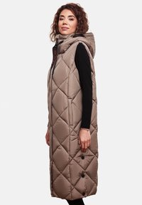 Long gilet beige matelassé avec une capuche, doté d'une fermeture éclair et de boutons sur le devant. Tissu texturé avec un motif en losanges.