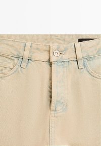 Jeans in denim beige con vita alta, tasche frontali e chiusura con zip e bottone in metallo, caratterizzati da un leggero effetto distressed.